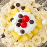 Banana Split Fluff dessert served in a bowl with bananas, marshmallows, and whipped topping, garnished with chocolate chips and maraschino cherries